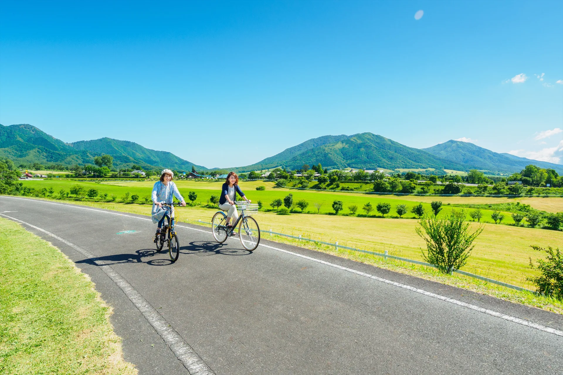 蒜山の山並みを背に、高原の道を自転車で走る2人